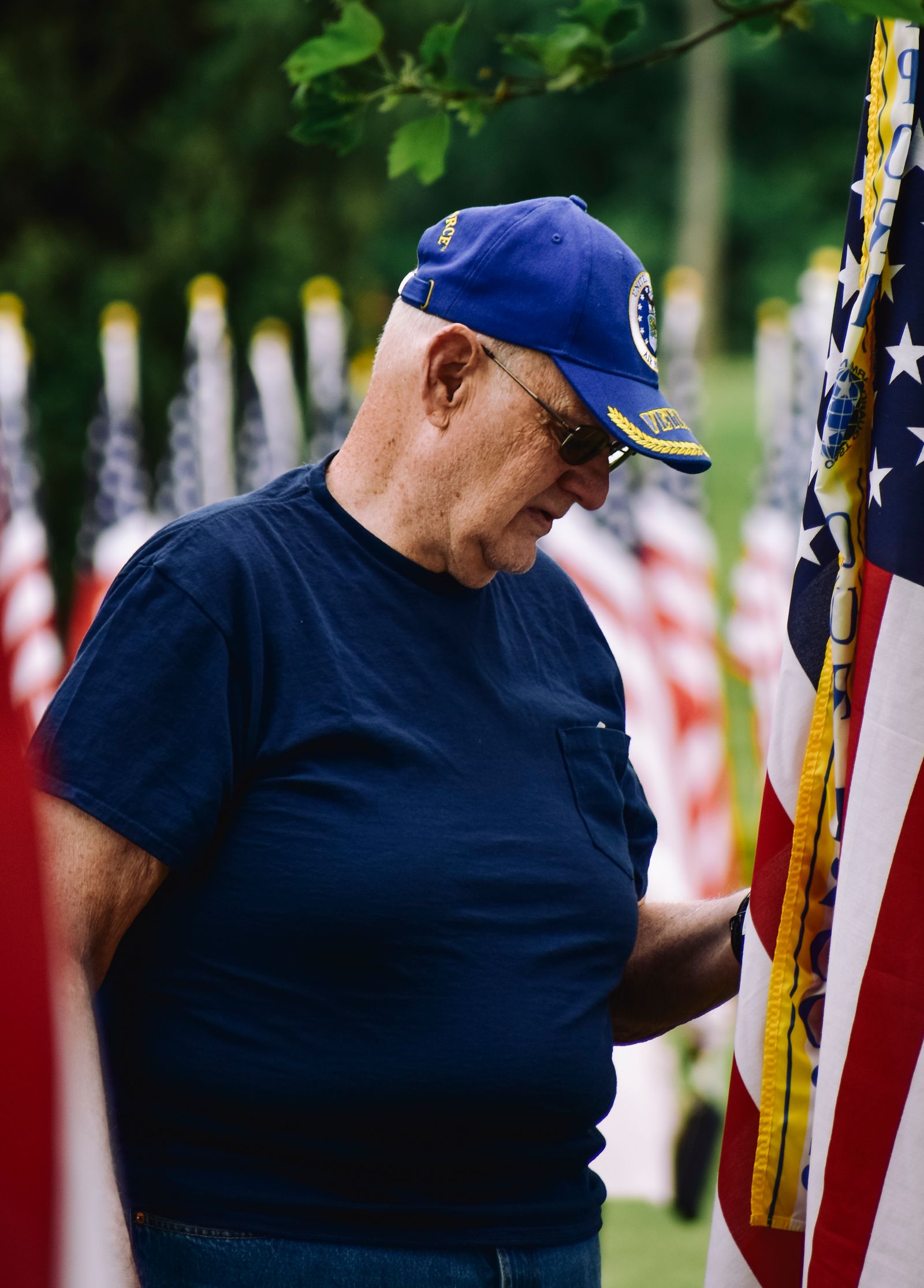 An older veteran in a service cap standing among American flags